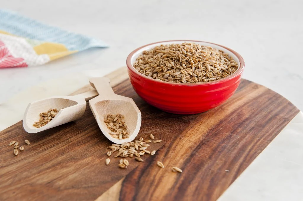 A bowl of BARLEYmax® wholegrain barley kibble on a wooden board with two wooden serving scoops.