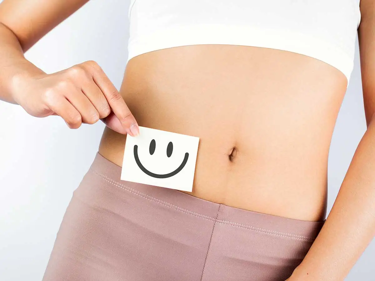 A young woman holding an image of a smiley face next to her tummy illustrating good gut health,